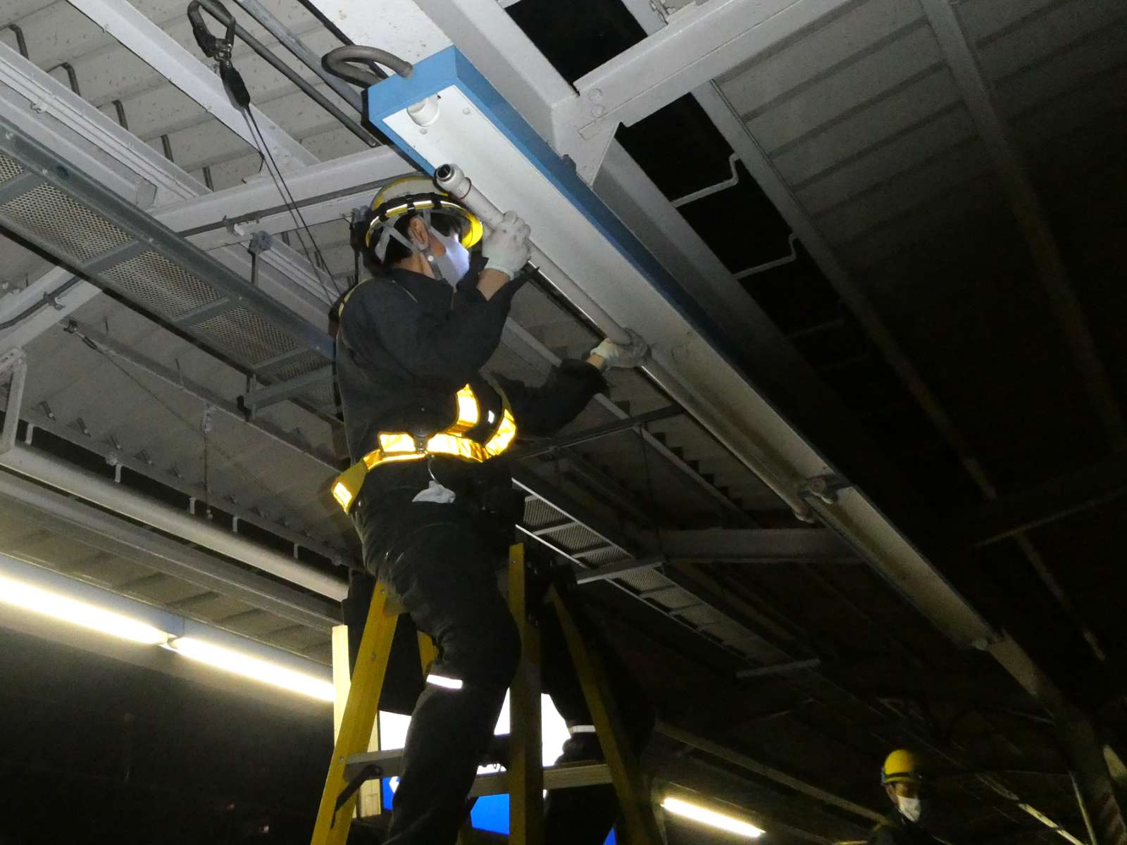 スタッフが脚立に登り、駅のホームの天井の電気を取り外している写真